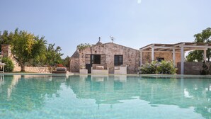 A clear swimming pool with a stone building and outdoor seating area in the background. - TD Trulli Della Lama Private Trulli With Pool (Castellana Grotte)
