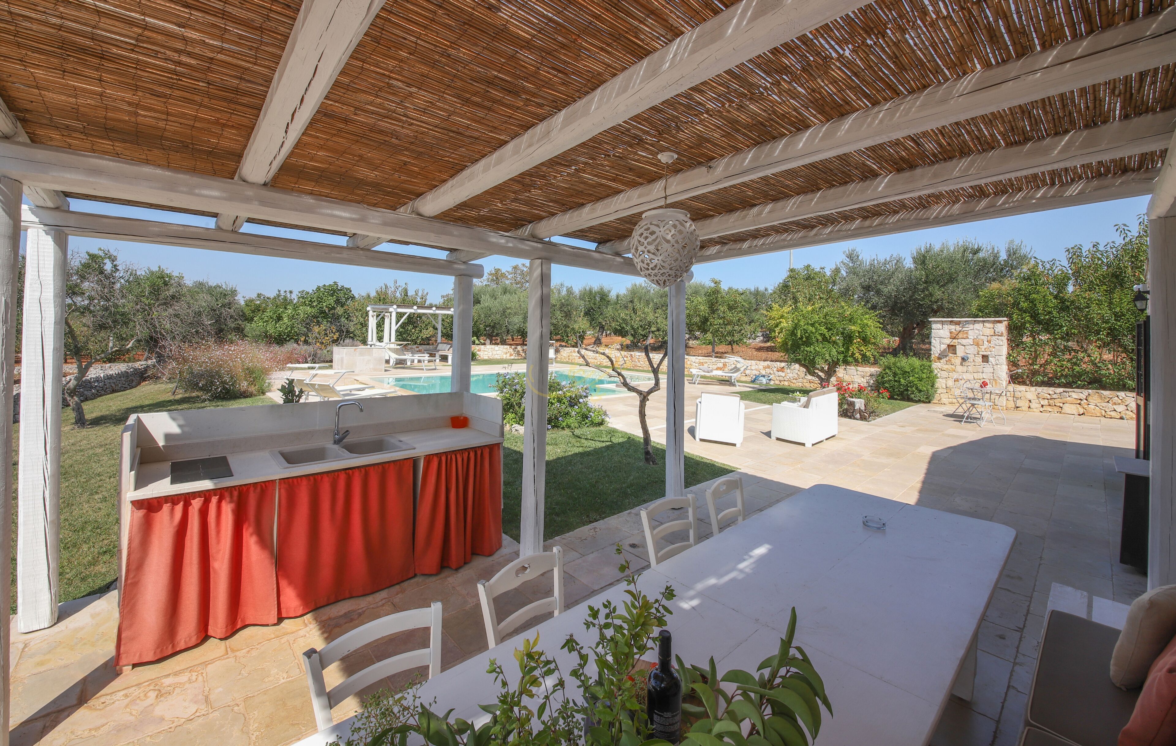 Un patio al aire libre con mesa, sillas, zona de barbacoa y vistas a una piscina y jardín.