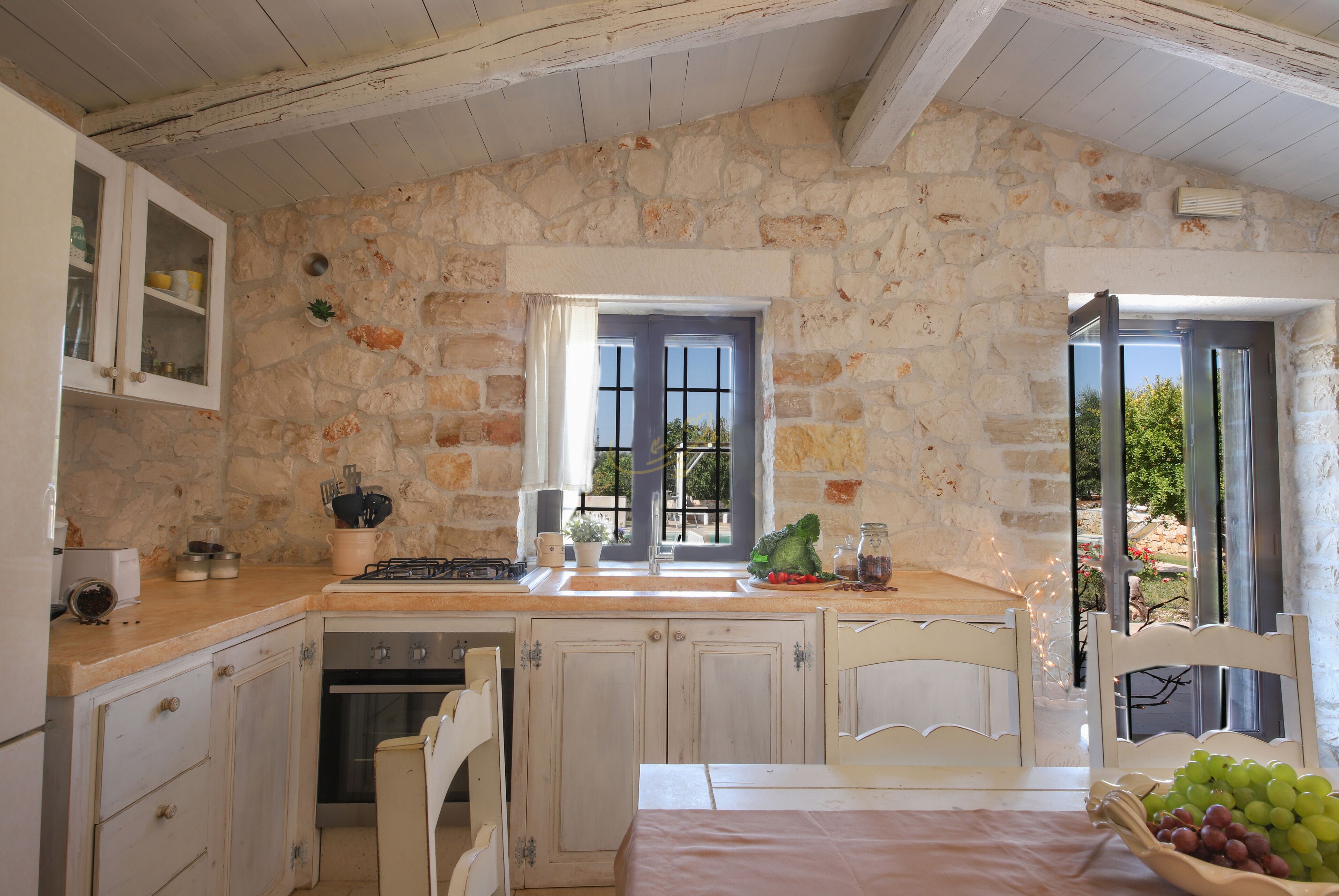 Una cocina rústica con paredes de piedra, armarios de madera y ventana con vistas a un jardín.