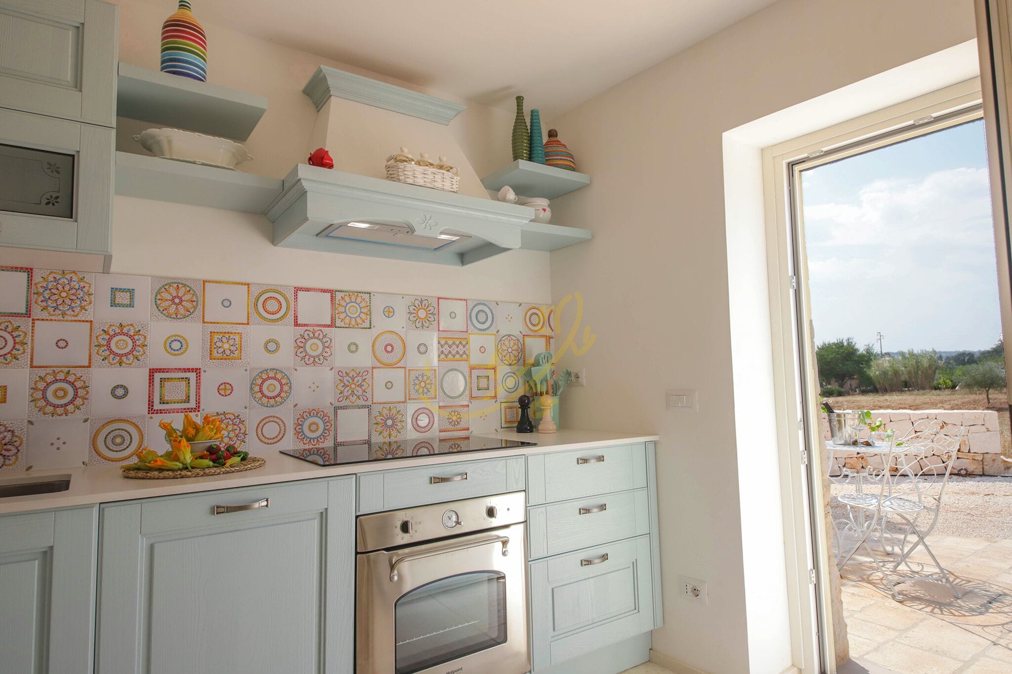 Una cocina con armarios azul claro, una estufa y un ventanal con vistas a un jardín.