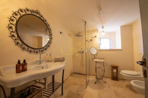 A bathroom with a large oval mirror, a sink, a toilet, and a shower area.