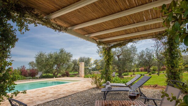 Ein überdachter Außenbereich mit Pool, Liegestühlen und einem Holztisch mit einem Weinglas.