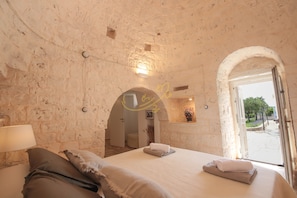 Ein Schlafzimmer mit Steinsturz, einem Bett mit Kissen, einem Nachttisch und einem Fenster mit offener Tür zum Außenbereich.