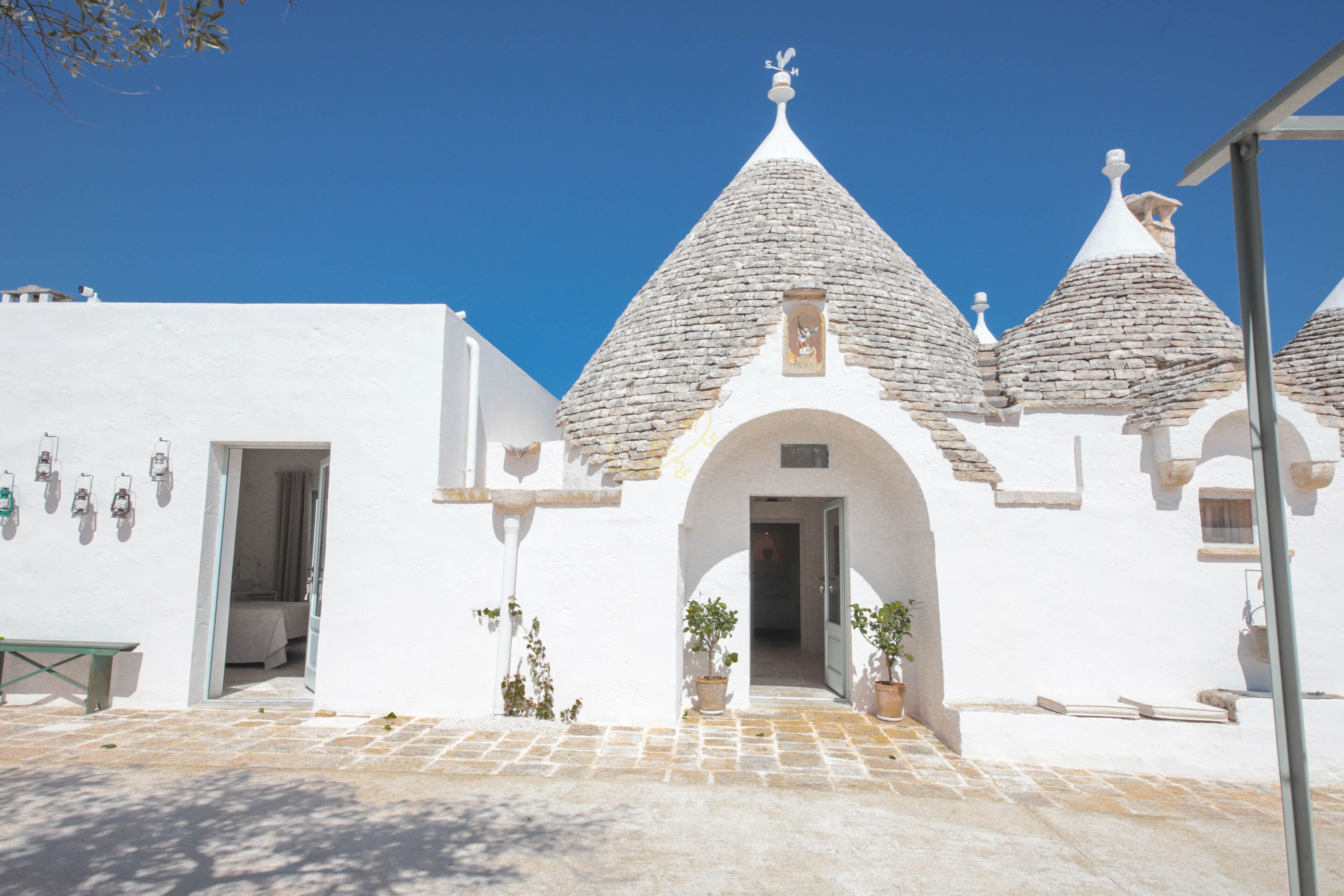 A white building with a stone roof, a doorway, and potted plants.
