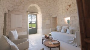 A cozy room with a white brick wall, a sofa, a chair, and a small table with candles and a book. - TD I Coni di Pinurè Trulli With Scenic Valley .. (Martina Franca)