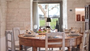 A rustic dining table set with plates, glasses, and a bottle, surrounded by white chairs in a room with exposed brick walls and a window with a view of greenery. - TD I Coni di Pinurè Trulli With Scenic Valley .. (Martina Franca)