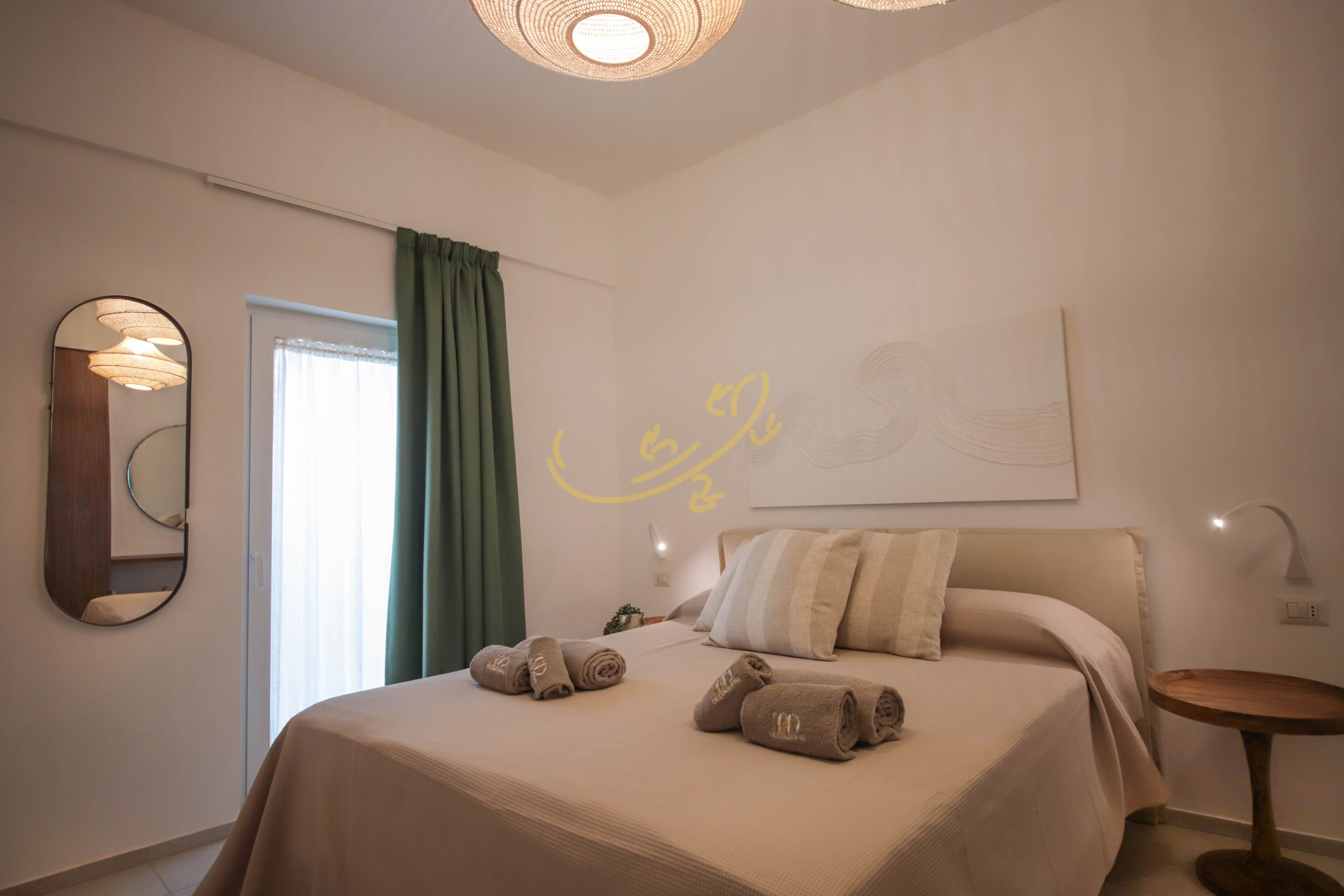 Una cama bien hecha con toallas, una lámpara de noche y un espejo montado en la pared en una habitación de hotel moderna.