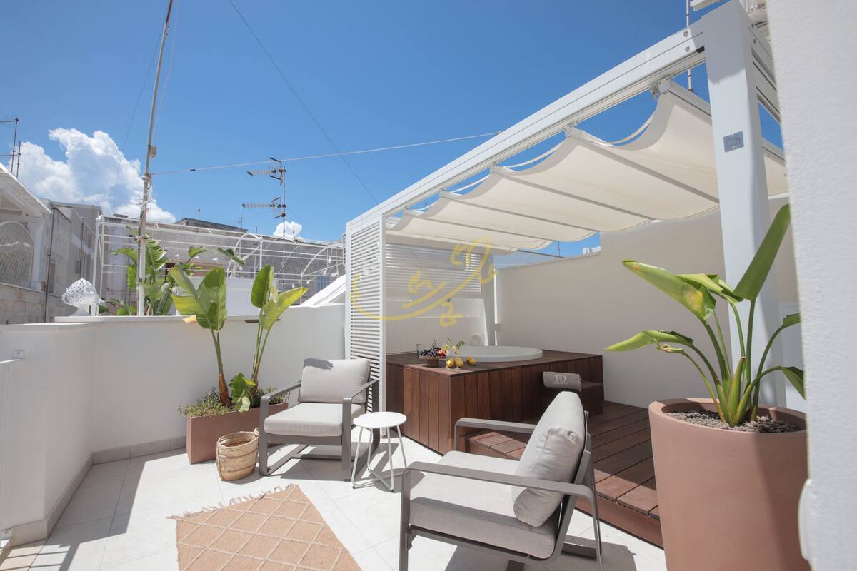 Eine sonnendurchflutete Terrasse mit Sitzgelegenheiten, einem kleinen Tisch und Kübelpflanzen.