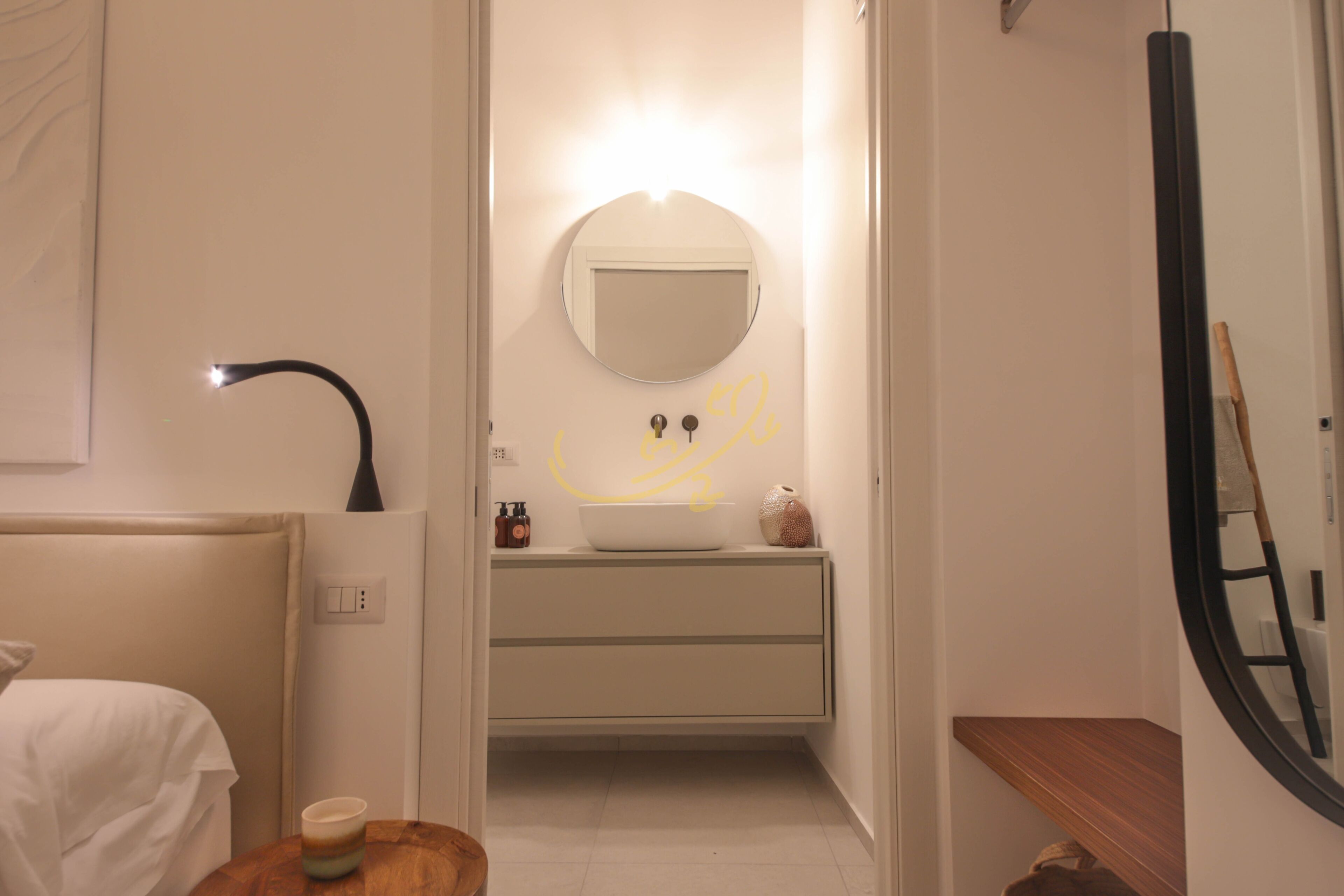 Un baño moderno con un espejo redondo, un lavabo y un banco de madera.