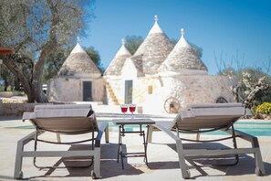 Two lounge chairs facing a stone building with conical roofs, a small table with two glasses, and a pool in the background. - TD Villa e Trulli il Bergamotto W/pool & Med/c.. (Ostuni)