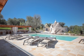Uma área de piscina com espreguiçadeiras, um pérgola e um edifício de pedra com telhados cônicos.