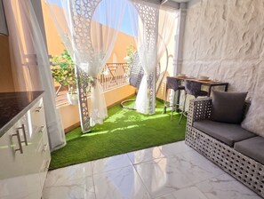A balcony with artificial grass, a cushioned seating area, and a dining table. - Romantic Apartment With Garden, Pool and Beach (Hurghada)