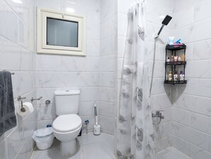 A bathroom with a toilet, a shower curtain, a toilet paper holder, a hand dryer, and a shelf with toiletries. - Romantic Apartment With Garden, Pool and Beach (Hurghada)