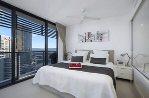 A modern hotel room with a large bed, a ceiling fan, a city view, and a minimalist decor. - Oracle Skyview | Luxury 26th Floor Ocean Escape (Gold Coast)