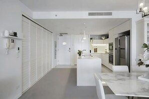 Una cocina moderna con armarios blancos, una isla central, iluminación colgante y encimera de mármol.