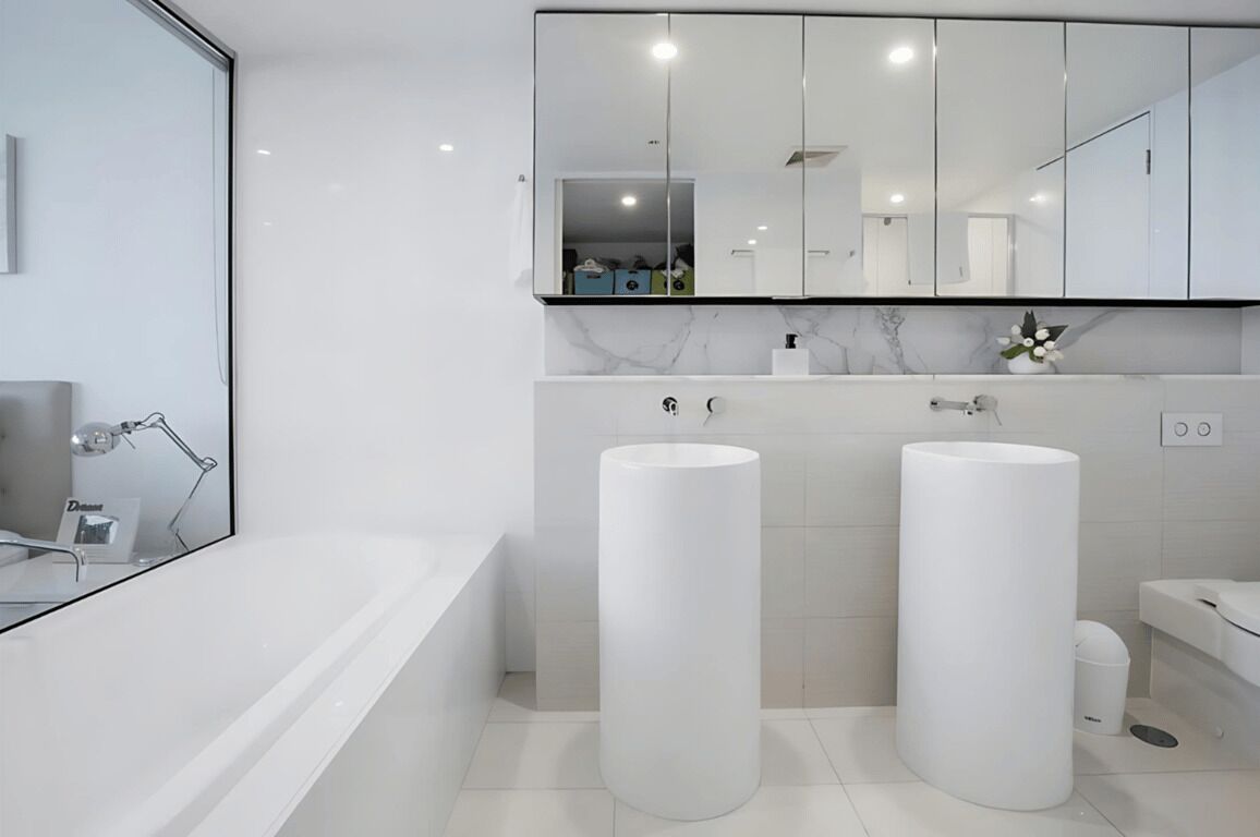 A modern bathroom with a large mirror, two sinks, and a bathtub.