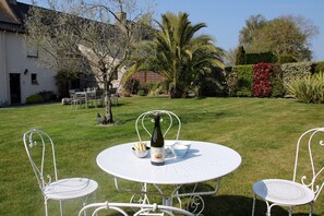 A white outdoor table with chairs, a bottle, and bowls, set in a grassy area with a building and trees in the background. - Le Mélorien by Archipel Evasion (Saint-Méloir-des-Ondes)