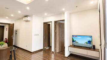 Una sala de estar moderna con un televisor de pantalla plana, un comedor con mesa y sillas, y un pasillo con puertas de madera.