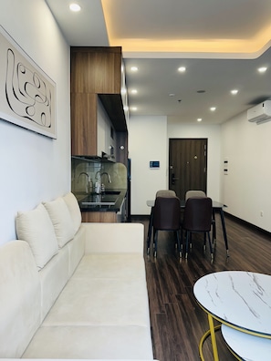 Una sala de estar moderna con un sofá, una mesa de comedor con sillas, una zona de cocina e iluminación empotrada en el techo.