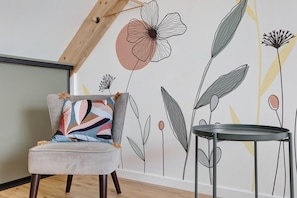 Une piĂšce avec un fauteuil gris, une table ronde et un mur ornĂ© dâune fresque florale.