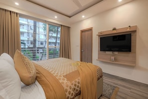 A hotel room with a bed, a TV mounted on the wall, a sliding door, and a view of buildings outside.