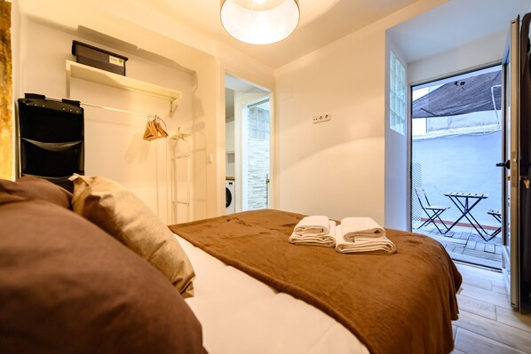 Ein Hotelzimmer mit Bett, Koffer, Handtuch und Blick ins Freie.
