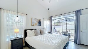 Ein Schlafzimmer mit Bett, Nachttischen, Deckenventilator, Fenster mit Vorhängen und Blick nach draußen.