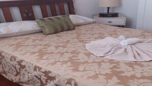 Un lit bien fait, avec une couvre-lit à motifs floraux, un oreiller vert et une serviette posée sur le côté.
