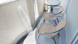 A balcony with two wicker chairs and a small round table, a white textured wall, and a metal railing. - Compact Easy Stay - Budget Nakasu (Fukuoka)