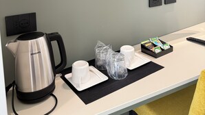 Une chambre d’hôtel moderne équipée d’une télévision à écran plat, d’une bouilloire, d’un plateau avec des tasses et des verres, et d’une petite table avec une télécommande.