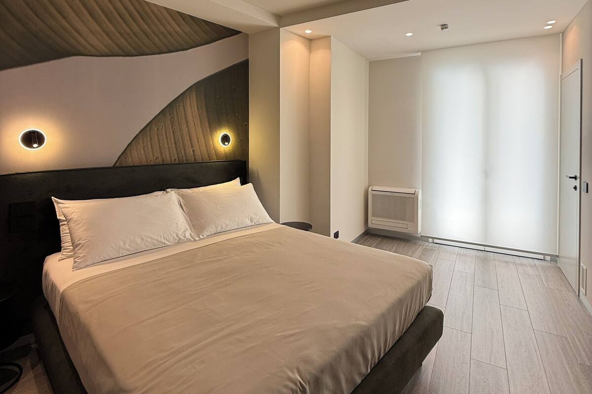 Un dormitorio moderno con una cama grande, cabecera con iluminación integrada, calentador de pared y vestidor.