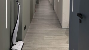 Un pasillo moderno con suelo de madera clara, paredes blancas y una puerta al final.