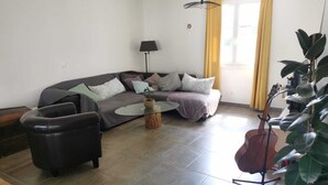 Un salon avec un canapé, une table basse, un fauteuil, une lampe, une guitare et une plante.