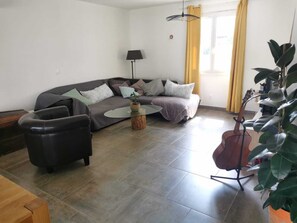Ein Wohnzimmer mit einer Couch, einem Couchtisch, einem Sessel, einer Lampe, einer Gitarre und einer Pflanze.