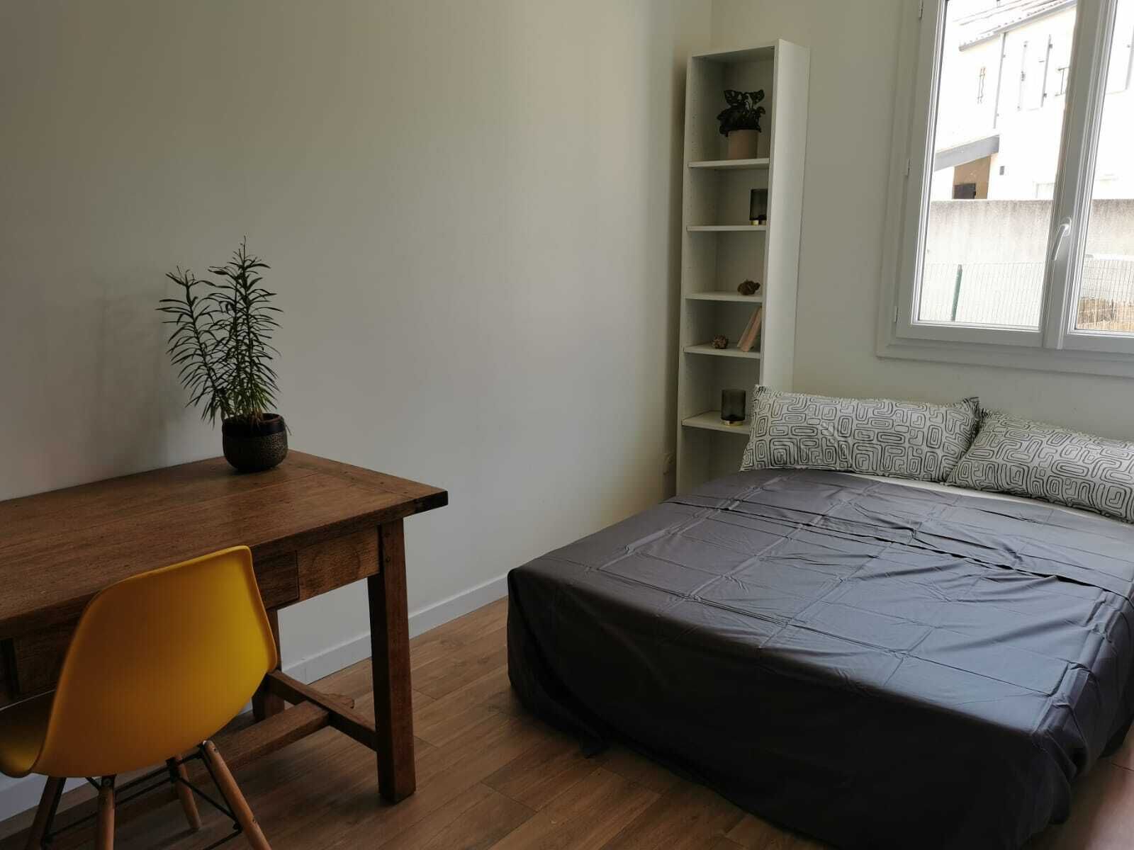 Ein Schlafzimmer mit einem Bett, einem Schreibtisch, einem Stuhl, einem Bücherregal und einem Fenster.