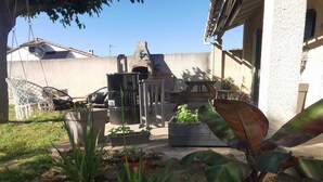 Une terrasse avec des meubles d’extérieur, un barbecue et un jardin agrémenté de diverses plantes et fleurs.