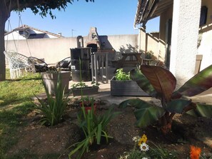Eine Terrasse mit Gartenmöbeln, einem Grill und einem Garten mit verschiedenen Pflanzen und Blumen.