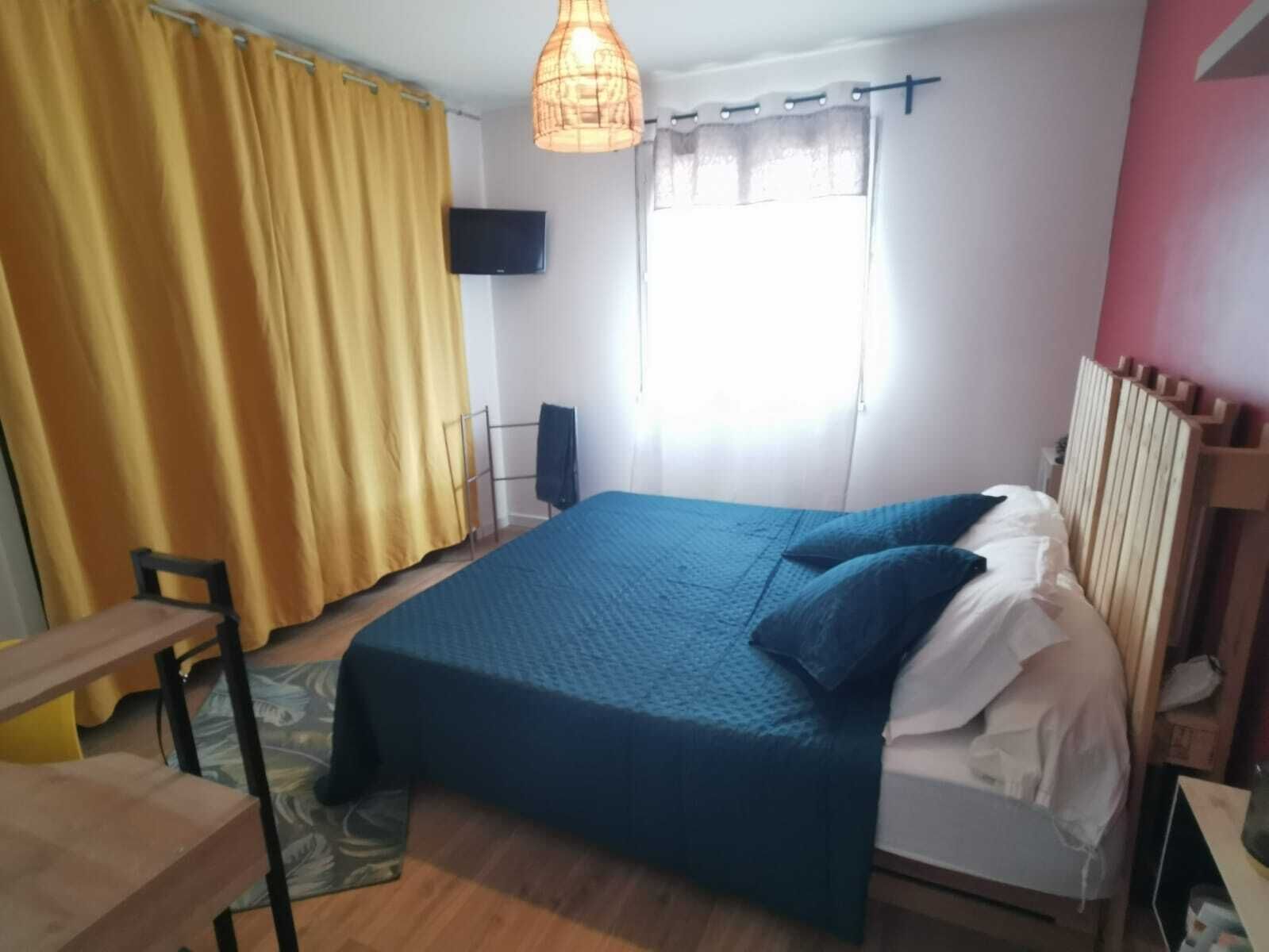 A bedroom with a bed, a chair, a standing speaker, and a window with curtains.