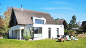 Ein modernes Haus mit Strohdach, großen Fenstern und einem gepflegten Rasen.
