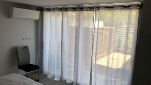 Een slaapkamer met een bed, een stoel, een raam met dunne gordijnen en een airconditioning.