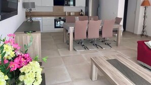 Een moderne keuken met witte kasten, een eethoek met een tafel en stoelen, en een aan de muur bevestigde televisie.