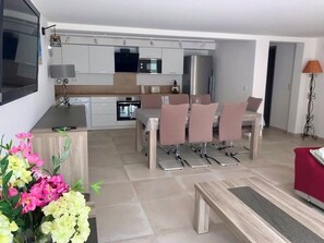 A modern kitchen with white cabinets, a dining area with a table and chairs, and a TV mounted on the wall. - 500 metres from the beach, air-conditioned, garden, swimming pool, ideal for families (Zonza)