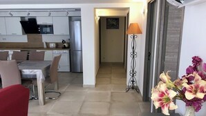 Een moderne keuken met roestvrijstalen apparatuur, een eethoek met tafel en stoelen, en een gang die naar een andere kamer leidt.