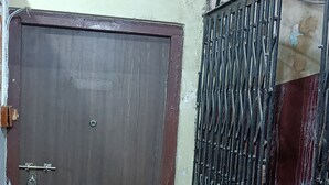 A closed wooden door with a metal gate, a concrete floor, and a patterned wall above. - Balaji Guest House (Guwahati)