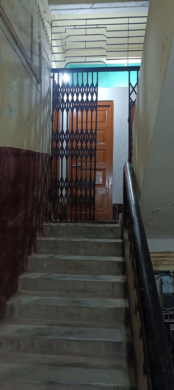 A staircase with a metal railing, a wooden door at the bottom, and a wall with peeling paint. - Balaji Guest House (Guwahati)