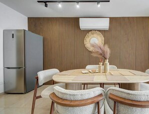A modern kitchen with a built-in refrigerator, a wooden wall panel, and a round dining table with chairs. - Beautiful 2BR seafront home with WIFI & comfy beds (Birżebbuġa)
