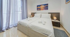 A hotel room with a large bed, two bedside tables, a painting on the wall, and sheer curtains. - Beautiful 2BR seafront home with WIFI & comfy beds (Birżebbuġa)