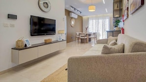 A modern living room with a flat-screen TV, a sofa, a dining area with chairs, and a kitchen counter. - Beautiful 2BR seafront home with WIFI & comfy beds (Birżebbuġa)