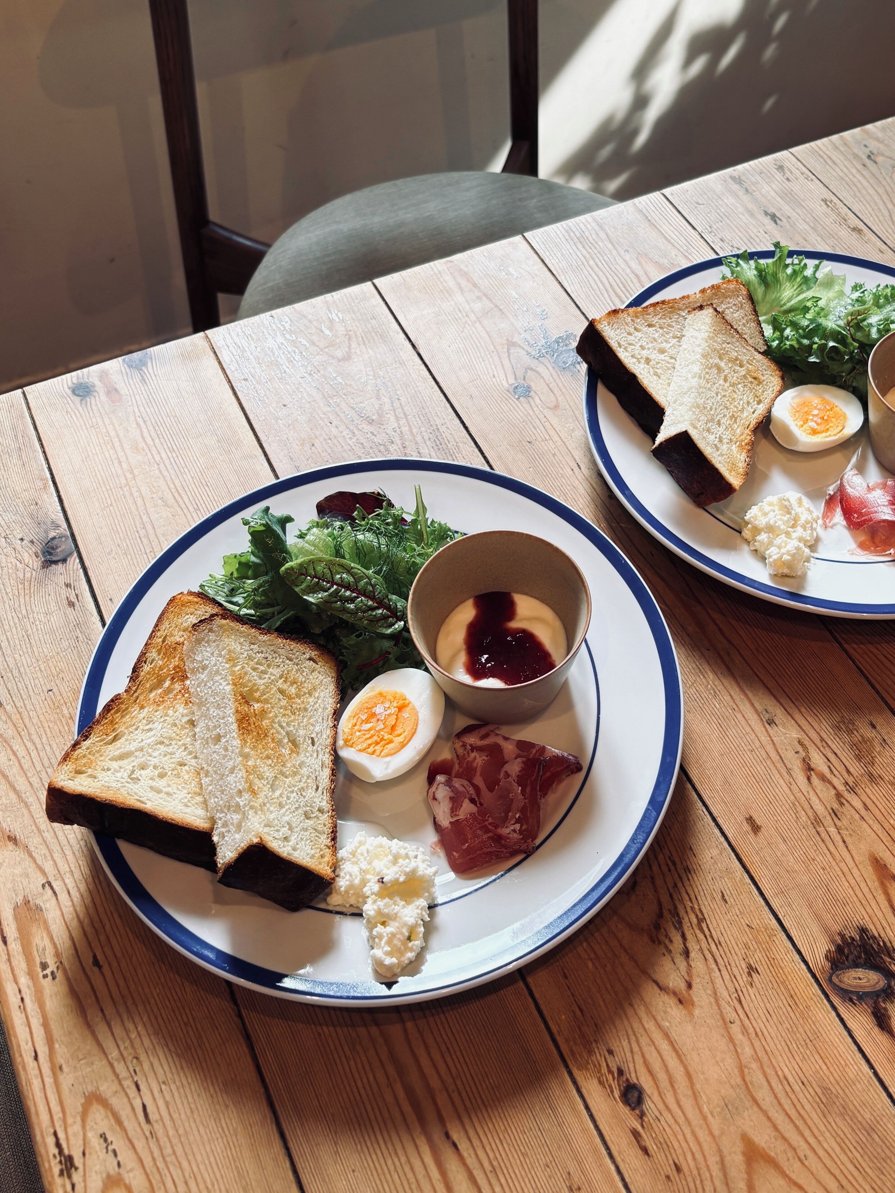 Dos platos de comida sobre una mesa de madera con borde azul, que incluyen tostadas, huevos, queso y verduras.