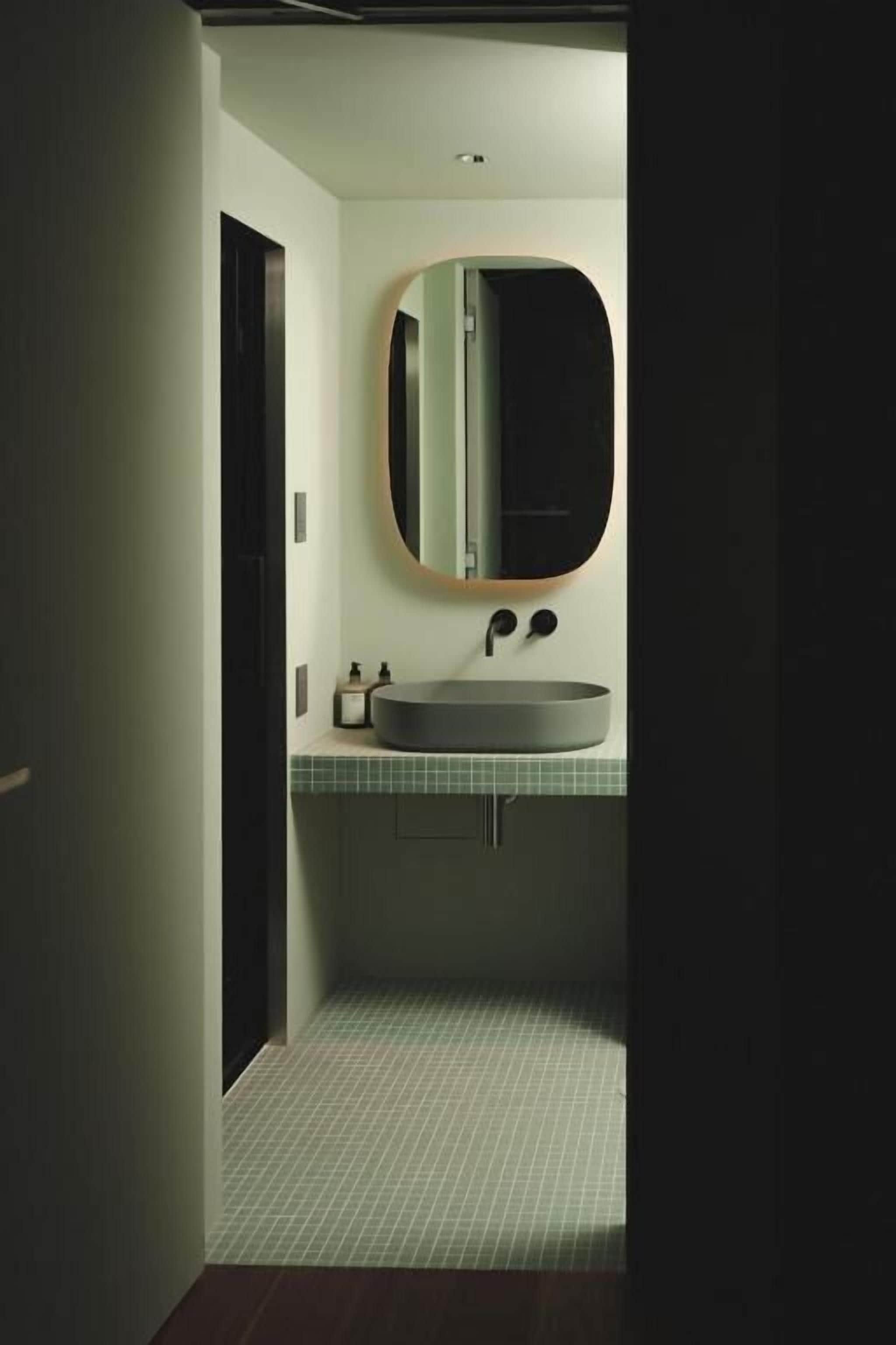 Een badkamer met een ronde spiegel, een wastafel en een betegelde vloer.